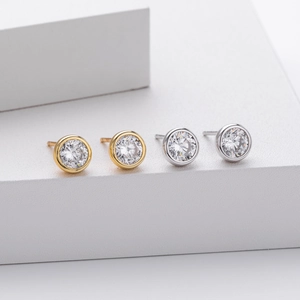 Detailed view of silver and gold bezel-set round zircon stud earrings on white podiums