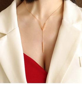 Detail of gold V-shaped and long bar pendant necklace worn on a model's neck