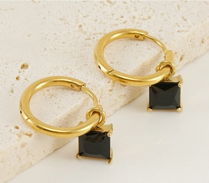 Close-up of golden stainless steel hoop earrings with black square zircon on beige stone
