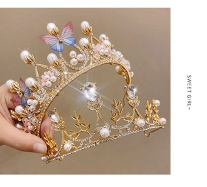 Close-up of golden crown with rhinestones, pearls and colorful butterfly decorations