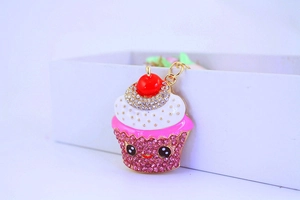 Detail of a cupcake keychain pendant with pink rhinestones and a red cherry topper