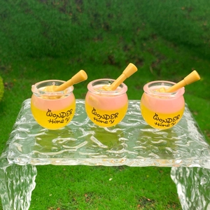 Three cute mini Wonder Honey pots in yellow and pink displayed on clear glass over grass