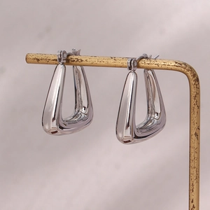 Close-up of chunky silver geometric hoop earrings on a metal display stand