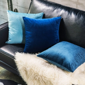 Three velvet pillow covers in blue shades displayed on a stylish sofa setup