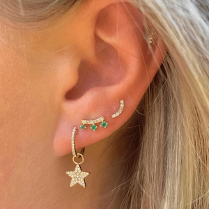 Detail of star-shaped earrings and green gemstone studs on a model ear