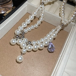 Detail einer doppelreihigen Perlenkette mit lila Zirkonia-Anhänger in Birnenform