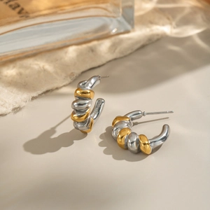 Two-tone silver and gold twisted C-shape hoop earrings on a minimalist warm background