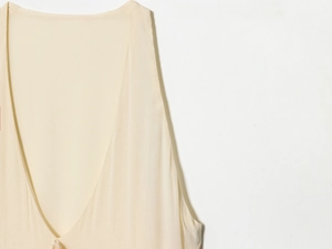 Detail of deep V-neck cream midi dress featuring elegant pleated chiffon texture