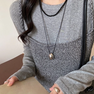 Close-up of a silver bean pendant on a black leather cord necklace worn by a model