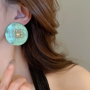 Détail d'une boucle d'oreille rétro verte avec perle centrale et rayons dorés fins