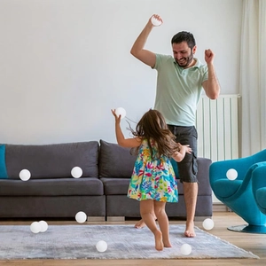 Father and daughter playing with glowing white Christmas snowball ornaments in cozy living room
