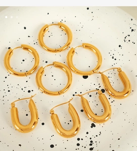 Detailed macro view of gold hoop and U-shaped earrings on a white marble display tray