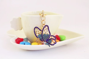 Detail of gold butterfly keychain with blue and purple rhinestones hanging on a white cup
