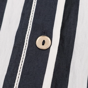 Close-up of black and white striped fabric with a premium golden metal button detail