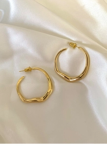 Detail of golden irregular round hoop earrings on white silk with a glossy metal finish