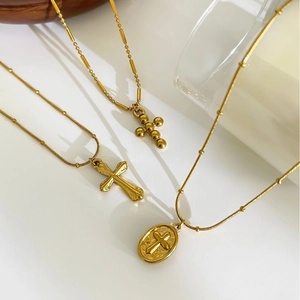 Three gold stainless steel cross necklaces with retro pendant on a minimalist background