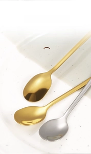 Detail showing gold and silver mirror polished stainless steel coffee spoons on ceramic plate