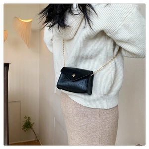 Detail of black faux leather crossbody bag with crocodile texture and gold chain strap