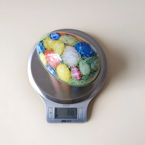 Tinplate Easter egg candy box showing a net weight of 66g on a digital kitchen scale