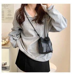 Model wearing a black woven leather bucket bag with drawstring and thin shoulder strap