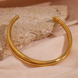 Detail of 18K gold-plated double-layer cross bangle on rock and silk background
