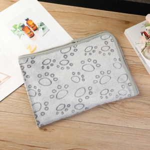 Close-up of a soft grey flannel pet blanket with dark paw prints on a wooden table