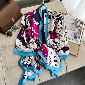 Elegant floral print silk scarf with blue borders displayed on a stylish beige sofa
