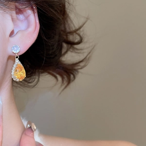 Close-up of sparkling gold water drop earrings with yellow gemstones worn on model