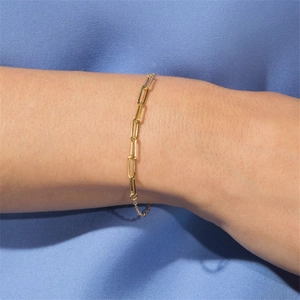 Detail of a gold-plated paperclip link bracelet on a wrist against blue silk