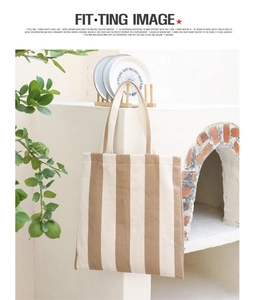 Detailed shot of brown striped canvas tote bag hanging by a stone wall with plants