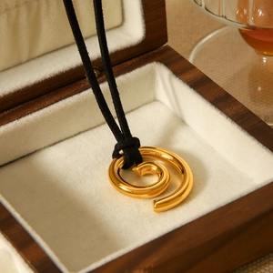 Macro shot of 18K gold spiral pendant on black cord inside a wooden jewelry box