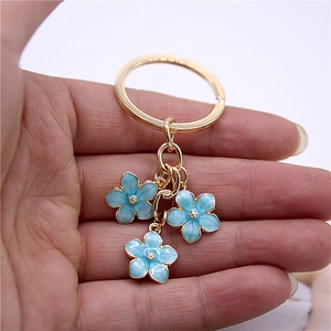 Close-up of gold-tone keychain with blue enamel flower pendants held in hand