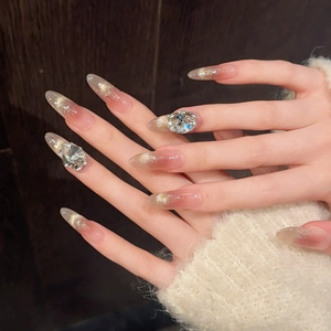 Detail of almond-shaped gradient pink press-on nails with large rhinestone and gold glitter