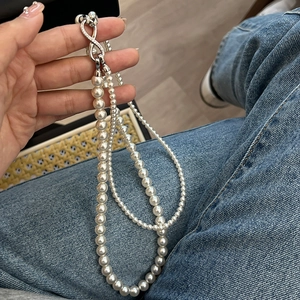 Close-up of white pearl necklace featuring a silver infinity clasp with zircon stones