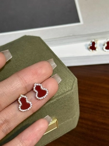 Detail shot of red gourd stud earrings with pavé crystals held against a green velvet box