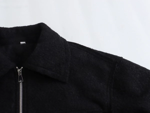 Détail de la veste en bouclé noire montrant la texture du tissu et le zip métallique