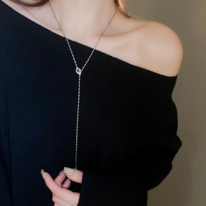 Close-up of silver Y-shaped necklace with green emerald-cut stone on model
