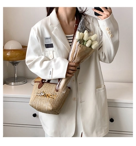 Detail of straw woven tote bag with tiger embroidery and brown handles held by a woman