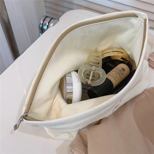 Macro view of white quilted cotton cosmetic bag showing metal zipper and large capacity interior