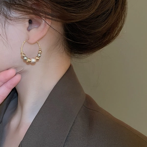 Close-up of contrast bead hoop earring with gold and silver spheres and a white pearl