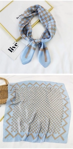 Detail of light blue and khaki checkerboard silk scarf folded and spread on a white surface