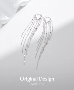 Macro detail of silver tassel earrings with heart-shaped clasps on white silk background