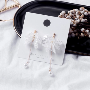 Detail of white flower petal earrings with pearls and gold chain on a branded display card