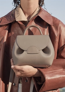 Detailed view of a small beige pebbled leather handbag held in front of a leather jacket