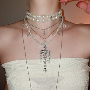 Close-up of double-layered necklace with pearl beads and diamond-studded cross pendants