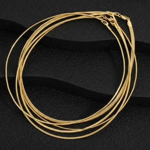 Macro detail of various 18K gold-plated snake and flat chains on a black textured background