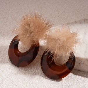 Detail view of tortoiseshell resin hoop earrings with beige faux fur pom poms on stone