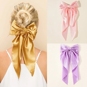 Detail of oversized satin bow hair clips in gold, pink, and purple glossy fabric