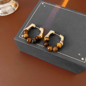 Detail of gold-plated earrings with tiger eye beads on a blue velvet jewelry gift box