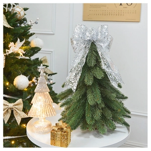 Mini green Christmas tree with silver sequin bow and glowing star lamp on a white table